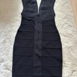 Svart klänning från Azim - Snygg svart klänning från Azim med djup v-ringning och breda axelband. Klänningen har en tight passform och är tillverkad i ett stretchigt material som ger en smickrande siluett. 