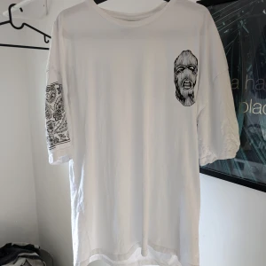 Vit oversized t-shirt från Black Squad - Säljer en vit oversized t-shirt från Black Squad med tryck av en maskerad figur på framsidan och texten 'CHAOTIC' på baksidan. T-shirten har korta ärmar och är tillverkad i bomull. Perfekt för en avslappnad stil.