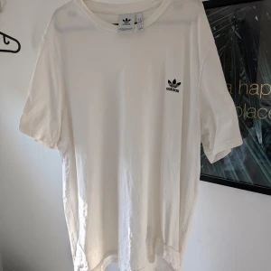 Vit t-shirt från Adidas - Säljer en klassisk vit t-shirt från Adidas med deras ikoniska logga tryckt på bröstet. T-shirten är kortärmad och tillverkad i mjuk bomull, perfekt för en avslappnad stil.