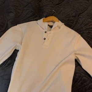 Vit/beige långärmad tröja med knappar - Säljer en stilren vit långärmad tröja med knappar vid halsen. Perfekt för en avslappnad look. Tröjan har en texturerad yta som ger den en unik känsla.