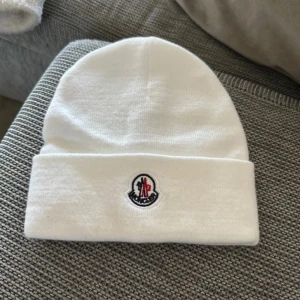 Vit mössa från Moncler - Snygg vit mössa från Moncler med broderad logga framtill. Perfekt för kyliga dagar och ger en stilren look. Tillverkad i mjukt material för extra komfort.
