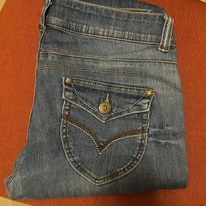 Blå bootcut jeans med dekorativa fickor - Svin snygga boot cut jeans 🤩. De är tyvärr lite för korta på mig, de är 79cm i inerbenslängd och 39cm tvärs över midjan. I super fint skick.
