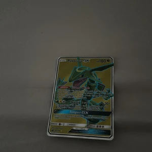Rayquaza GX Pokémonkort - Säljer ett Rayquaza GX Pokémonkort med HP 180. Kortet har förmågan Stormy Winds och attackerna Dragon Break och Tempest GX. Perfekt för samlare eller spelare som vill förstärka sin kortlek med en kraftfull drake.