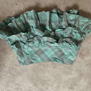 Grön rutig kjol med volanger - Snygg grön rutig kjol med flera volanger som ger en lekfull look. Perfekt för att sticka ut med sitt unika mönster och design. Kjolen har en kort längd och är tillverkad i ett lätt material som passar bra för varmare dagar.