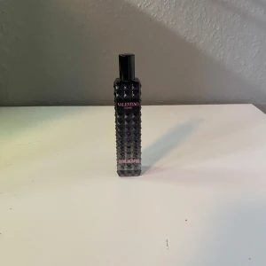 Valentino Uomo parfym - Säljer en elegant Valentino Uomo parfym i en stilren svart flaska med nitar. Perfekt för den som vill ha en sofistikerad doft med en touch av lyx. Flaskan är smidig och lätt att ta med sig. 7ml kvar
