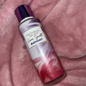 Love Spell Radiant från Victoria's Secret - Fräsch och förförisk doftmist från Victoria's Secret, Love Spell Radiant. Flaskan är dekorerad i lila och rosa toner med en elegant design. Perfekt för att ge en extra touch av glamour till din dag.