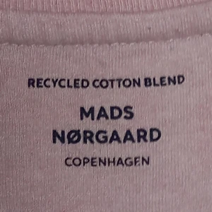 Rosa t-shirt från Mads Nørgaard - Säljer en stilren rosa t-shirt från Mads Nørgaard. Tillverkad i en återvunnen bomullsblandning med korta ärmar och en diskret logga på bröstet. Perfekt för en avslappnad look.