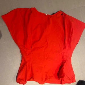 Röd topp från Zara - Säljer en snygg röd topp från Zara. Den har en lös passform och korta ärmar, perfekt för en avslappnad stil. Toppen är tillverkad i ett lätt material som gör den bekväm att bära.