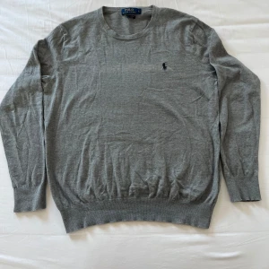 Grå tröja från Polo Ralph Lauren - Säljer en stilren grå tröja från Polo Ralph Lauren i slim fit. Tröjan har långa ärmar och en liten broderad logotyp på bröstet. Perfekt för en klassisk och elegant look. Den är i storlek L men passar även M. OBS en missfärgning mitt på tröjan annars i bra skick 