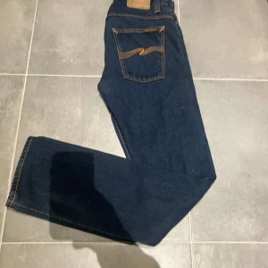Mörkblå jeans från Nudie Jeans - Snygga mörkblå jeans från Nudie Jeans med klassisk femficksdesign och orange sömmar. Jeansen har en normal passform och är tillverkade i högkvalitativt denim. Perfekta för en stilren look.