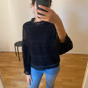 Svart spetsblus - Säljer en elegant svart spetsblus med långa ärmar och vackra detaljer. Blusen har ett unikt mönster med cirklar och en fin kant vid halsen.  Som ny (spegeln är smutsig och inte varan) 