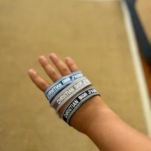 3 st olika färger Christian Dior J'adior armband set - Säljer tre snygga Christian Dior J'adior armband i blått, grått och svart. Armbanden är vävda med tydlig logga och har coola tofsar i matchande färger. Perfekt accessoar för att lyfta din outfit med en lyxig touch och streetkänsla.