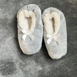Grå fluffiga tofflor med rosett - Supermysiga grå tofflor från Female Passion med vit fluffig insida och söt rosett framtill. Perfekta att glida runt i hemma när du vill ha det extra bekvämt. Mjukt material och halkfri sula för bästa komfort.