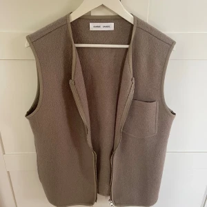 Beige ullväst från Samsøe Samsøe - Stilren beige väst i ull från Samsøe Samsøe med rak passform. Västen har en praktisk bröstficka och stängs med en grov dragkedja framtill. Perfekt lager-på-lager-plagg med diskreta kantband och minimalistisk look. Nypris 2000.