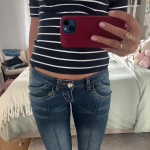 Lågmidjade blå bootcut jeans - Säljer ett par blå lågmidjade jeans med bootcut-snitt och snygga detaljerade fickor. Jeansen har markerade sömmar framtill och cool grön brodyr på bakfickan. Perfekta för dig som gillar en retro vibe och vill sticka ut lite extra. Skulle säga att de passar en 36 eller 38 💕💕