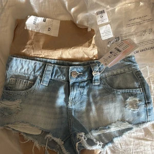 Lågmidjade jeansshorts från Gina Tricot - Lågmidjade jeanshorts me detaljer på bakfickorna. Korta i längden. Helt oanvända , glömde lämna tillbaka bara. Lapp kvar.  Från gina 14+.