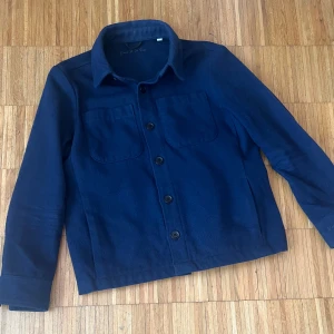 Mörkblå overshirt från Donce De La Sense - Overshirt i mörkblå ull från Donce De La Sense. Klassisk rak modell med två stora bröstfickor, knäppning framtill och mjuk känsla. Perfekt att slänga över en t-shirt för en chill look. Snygg broderad logga på ärmen.