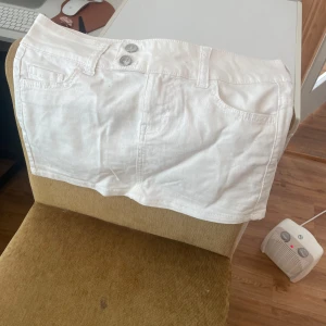 Vit jeanskjol med fickor - Snygg vit kort jeanskjol med klassiska fickor fram och dubbla knappar i midjan. Perfekt för dig som vill ha en fräsch och enkel look till sommaren. Kjolen har bälteshällor och en rak passform.