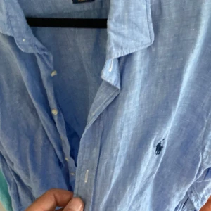 Blå linneskjorta Polo Ralph Lauren - Snygg blå skjorta från Polo Ralph Lauren i slim fit-modell. Tillverkad i svalt linne med klassisk krage, knappar framtill och ikoniska broderade loggan på bröstet. Perfekt för dig som gillar stilrena och bekväma plagg med premiumkänsla.