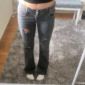 Grå bootcut jeans med slitningar - Säljer ett par grå jeans med bootcut-modell och snygga slitningar på benen. Jeansen har låg midja, klassiska fickor och dragkedja fram. OBS Jag har klippt hålen själv. 💕