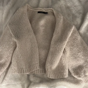 Beige stickad kofta från Vero Moda - Mysig beige stickad kofta från Vero Moda. Koftan har en öppen front utan knappar. Tjockt, fluffigt garn 