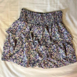 Blommig kjol från Vero moda - Supersöt blommig, kort kjol från Vero moda. Lila, gula och gröna blommor. Stretchig i midjan. Storlek S. Mycket fint skick! Endast använd ett fåtal gånger.