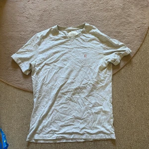 Grå t-shirt - Snygg ljusgrå t-shirt från Les Deux med röd broderad II-logga på bröstet. Klassisk passform, rund hals och korta ärmar. Tillverkad i mjuk bomull som känns skön mot huden. Perfekt för en clean och stilren look!🙌🏻
