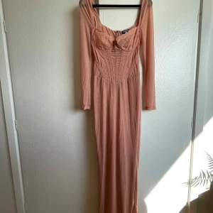 Lång rosa spetsklänning PrettyLittleThing - Supersnygg långklänning i ljusrosa från PrettyLittleThing med figurnära passform, långa ärmar och spetsdetaljer vid bysten. Klänningen har markerad midja, mesh-tyg och dragkedja bak. Perfekt för dig som vill sticka ut med en elegant och feminin look.