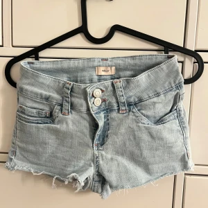 Ljusblå jeansshorts från Nelly - Ljusblåa jeansshorts från Nelly med rosa detaljer. De är aldrig använda men tvättade en gång. Lågmidjade i storlek 32