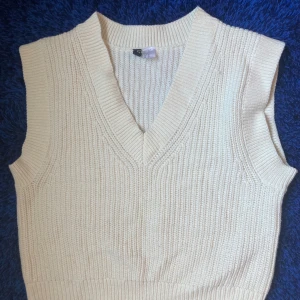 Vit stickad väst från Divided XS, H&M - Säljer en beige stickad väst från Divided H&M i storlek XS. Västen har v-ringning och bred ribbad kant vid hals och ärmhål. 
