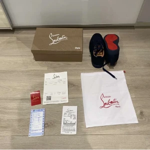 Mörkblå sneakers från Christian Louboutin - Snygga mörkblå sneakers från Christian Louboutin med klassisk röd sula och diskret logga. Skorna har rund tå, snörning och är tillverkade i mocka med läderdetaljer invändigt. Perfekta för dig som vill sticka ut med exklusiv stil och ikoniska detaljer.