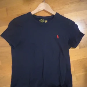 Mörkblå t-shirt från Polo Ralph Lauren -  Stolekn e xs i man så den sitter som S i tjej Snygg mörkblå t-shirt från Polo Ralph Lauren med klassisk röd broderad logga på bröstet. T-shirten har rund halsringning och korta ärmar. Perfekt basic-plagg med stilren vibe och skön passform i mjuk bomull.