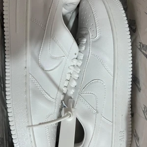 Vita Nike Air Force 1 - Nike Air Force 1 sneakers i helvitt skinn med klassisk siluett och perforerad tå. Snygga detaljer som metallbricka på snörningen och tydlig Nike-logga på sidan.