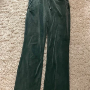 Mörkgröna mjukisbyxor i sammet - Mörkgröna mjukisbyxor i mjuk sammet med raka ben och dragsko i midjan. Byxorna har två fickor fram och två bakfickor. Perfekta för chill dagar eller när du vill vara extra bekväm. Har en liten fläck på ens benet