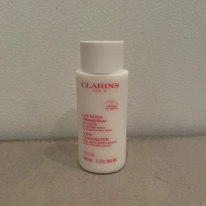 Clarins Velvet Cleansing Milk 100ml - Clarins Velvet Cleansing Milk i en vit plastflaska med röd text, 100 ml. Innehåller extrakt av alp-gentiana och citronmeliss. Perfekt för att ta bort smink och rengöra huden på ett skonsamt sätt.