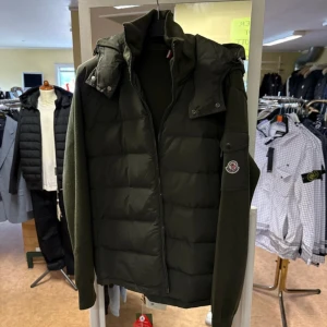 Grön pufferjacka från Moncler - Snygg mörkgrön pufferjacka från Moncler med stickade ärmar och klassisk logga på armen. Jackan har dragkedja framtill, hög krage och quiltad front. Perfekt för dig som vill ha en stilren och varm jacka med exklusiv känsla.