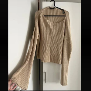  ribbstickad tröja med vida ärmar - Säljer en beige ribbstickad tröja med rund halsringning och långa, vida ärmar. Tröjan har en avslappnad passform och är perfekt för lager-på-lager.