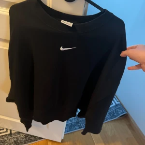 Nike sweatshirt - Svart sweatshirt från Nike med klassisk broderad vit swoosh-logga på bröstet. Tröjan har rund halsringning och långa ärmar, perfekt för en sportig och avslappnad stil. Tillverkad i mjuk bomullsmix som är skön att bära.