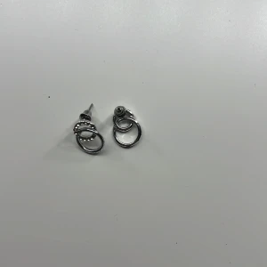 Silvriga örhängen med dubbla ringar - Snygga silvriga örhängen med två sammanlänkade ringar, där den ena ringen är dekorerad med små glittrande stenar. Perfekta för att ge din look lite extra bling och stil. Passar dig som gillar minimalistiska men ändå iögonfallande smycken.