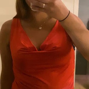 Röd satinlinne från NA-KD - Säljer ett rött linne från NA-KD i glansig satin med snygg drapering vid urringningen. Modellen är ärmlös och har en figurnära passform som ger en trendig look. Perfekt för dig som vill sticka ut med färg och stil.