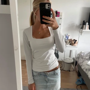 Vit långärmad topp med fyrkantig ringning - Snygg vit långärmad topp med fyrkantig ringning och figurnära passform. Perfekt att styla med jeans eller kjol för en clean look. Mjuk och stretchig, troligtvis i bomullsmix. Enkel och stilren design som passar året runt.