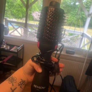 Revlon One-Step Volumizer hårborste - Revlon One-Step Volumizer är en svart och rosa elektrisk rundborste med borst i plast och piggar med rosa toppar. Perfekt för att styla och ge volym till håret samtidigt som du fönar det. Ergonomiskt handtag och flera värmelägen för enkel styling.