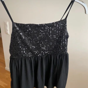 Svart paljetttopp  - Supersnygg svart kortklänning från Gina Tricot med smala axelband och glittrig paljettöverdel. Kjolen är luftig och har en lätt rynkad effekt. 