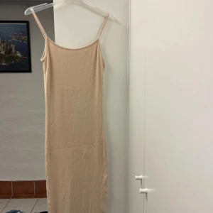 Beige ribbad långklänning från Amisu - Snygg beige långklänning från Amisu med smala axelband och ribbad struktur. Klänningen är figurnära och har en slits nertill för extra rörelsefrihet. Perfekt för dig som gillar minimalistisk och stilren look.