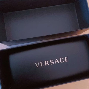 Svarta Versace solglasögon med guld - Snygga svarta solglasögon från Versace med kantig form och coola guldiga Medusa-detaljer på sidorna. Glasögonen har mörka linser och kommer med originaletui och certifikat. Perfekt accessoar för att sticka ut.