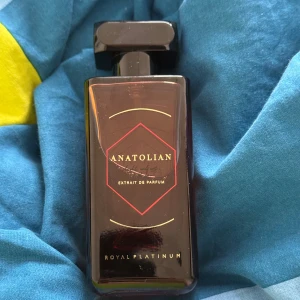 Anatolian Royal Platinum Parfym - Exklusiv parfymflaska från Anatolian, Royal Platinum Extrait de Parfum. Flaskan är rektangulär i mörkbrunt glas med svarta och guldiga detaljer samt röd geometrisk design. Lyxig och stilren look som passar perfekt på parfymhyllan.