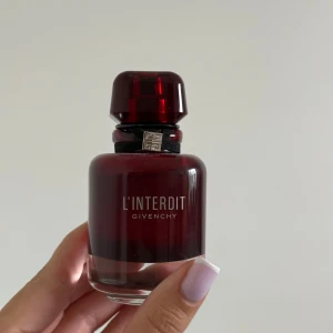 Givenchy L'Interdit parfym röd flaska - Givenchy L'Interdit parfym i en elegant, mörkröd glasflaska med svart band och silverdetalj vid halsen. Flaskan har en rundad form och ett stilrent lock i samma röda nyans. Perfekt för dig som gillar lyxiga och ikoniska dofter. 50ml