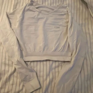 Vit croppad tröja från ICANIWILL - Säljer en vit croppad långärmad tröja från ICANIWILL. Tröjan har en enkel design med diskret logga på bröstet och bred mudd nertill. Perfekt för träning eller chill dagar. Materialet är mjukt och stretchigt, vilket gör den riktigt skön att bära.