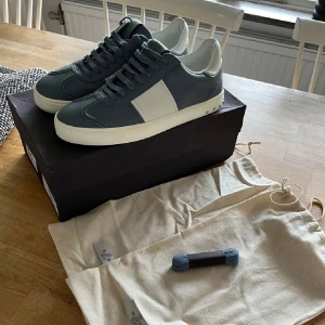 Valentino Garavani sneakers blå/vit - Snygga sneakers från Valentino Garavani i blått och vitt skinn med klassiska nitar baktill. Modellen har rund tå, platt sula och bred vit panel på sidan. Skorna har snörning och kommer med extra skosnören och dustbags. Perfekta för dig som gillar exklusiv streetstyle.