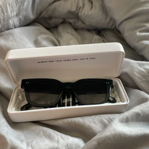 Svarta solglasögon från Chimi - Snygga svarta solglasögon från Chimi med bred, fyrkantig båge och mörka glas. Klassisk och stilren design med två silverprickar på varje sida av bågen. Kommer i original box med putsduk.